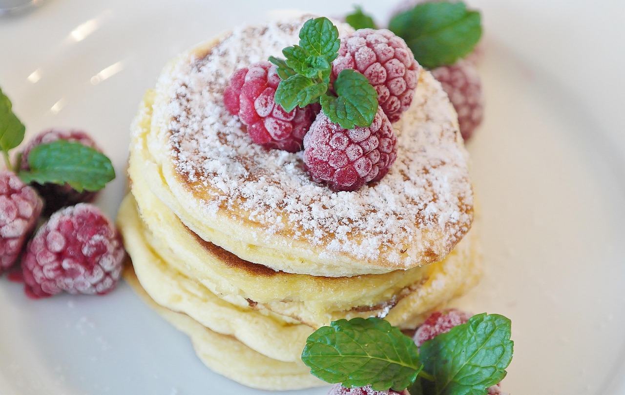 Pancakes dusted with powdered sugar under raspberries and mint