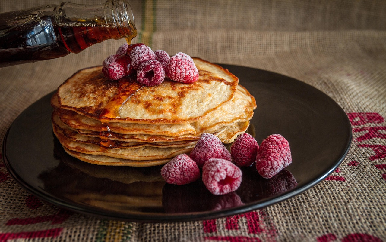 Maple syrup pouring over a stack of pancakes topped with raspberries